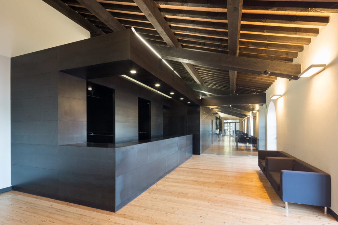 Lungo bancone bar dal design moderno in metallo scuro, contrasto con l'architettura storica