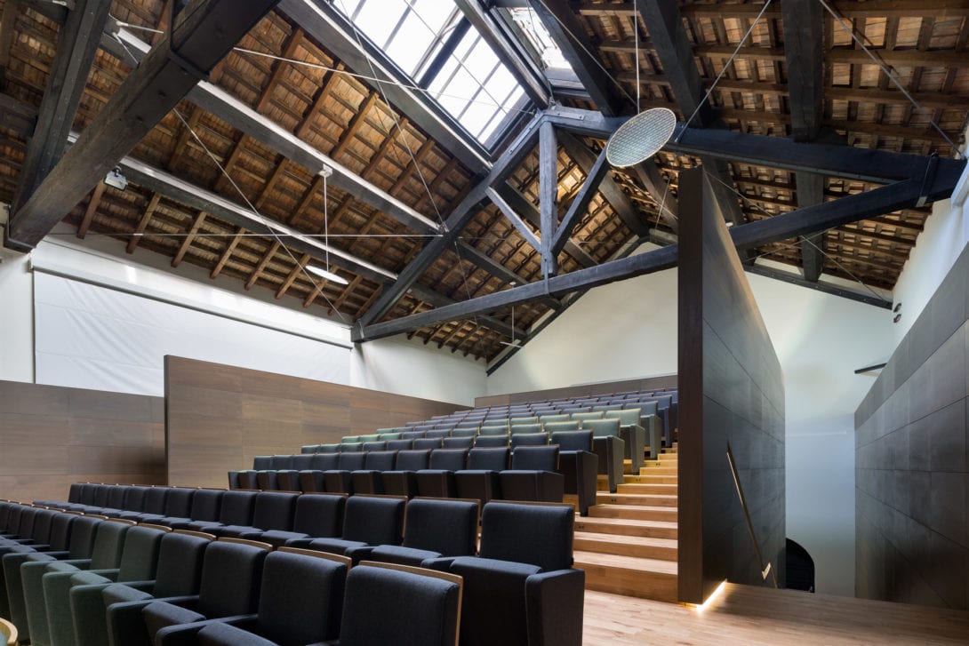 Sedute nere del teatro a netto contrasto con la copertura storica in legno e tiranti in acciaio