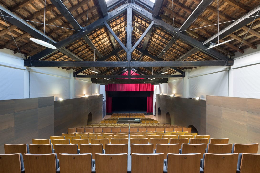 Vista simmetrica verso il palcoscenico con sipario rosso, fotografo interni architettura industriale Toscana